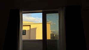 Una habitación con un ventanal grande, vista a un edificio amarillo y una malla protectora.