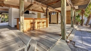 Un espace extérieur abrité avec un plancher en bois, un bar avec des tabourets et une vue sur une maison en arrière-plan.