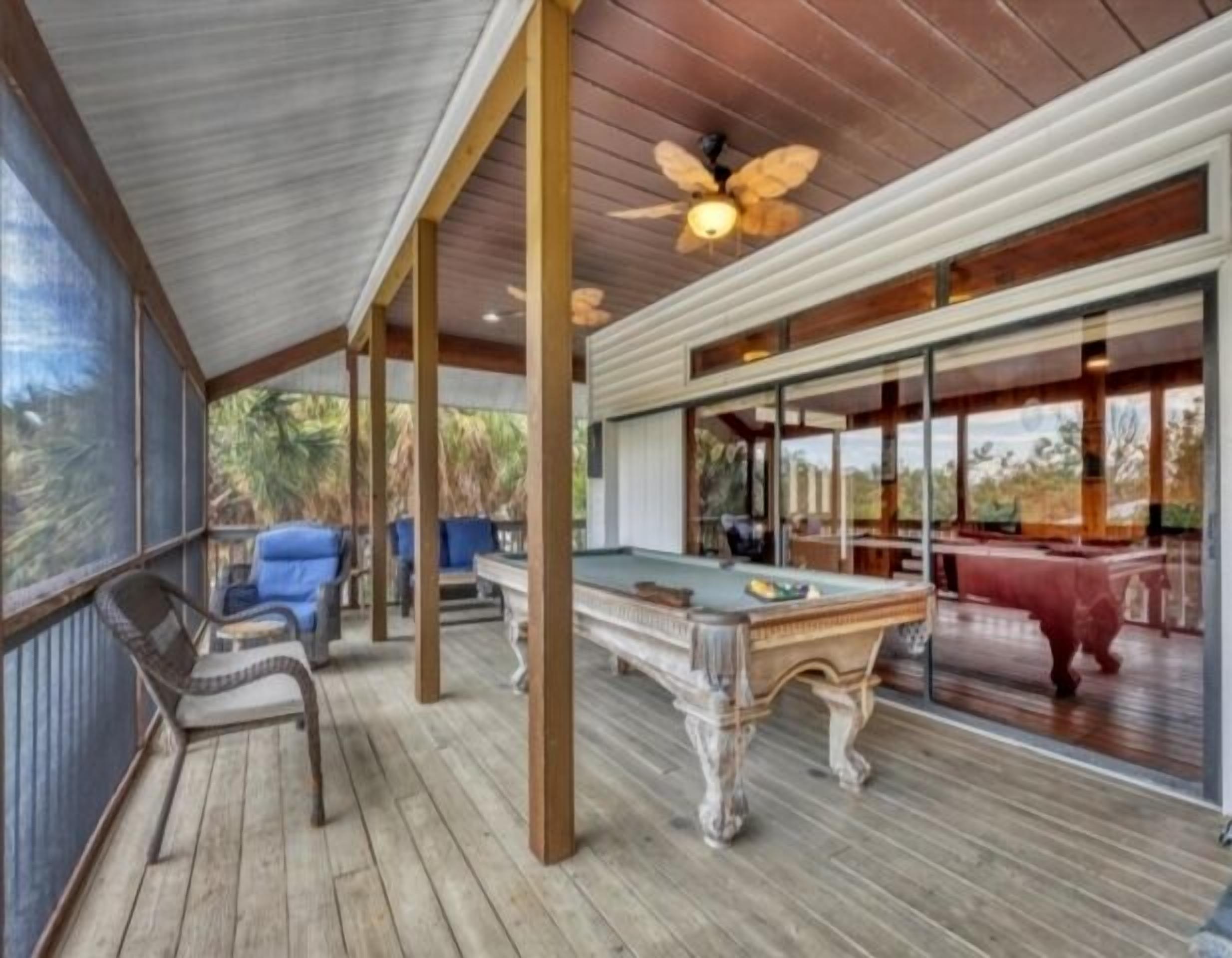 A covered outdoor area with a pool table, chairs, and a ceiling fan.