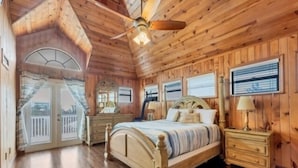 Une chambre dans une cabane en bois, avec un lit, des tables de chevet, une commode et un ventilateur de plafond.