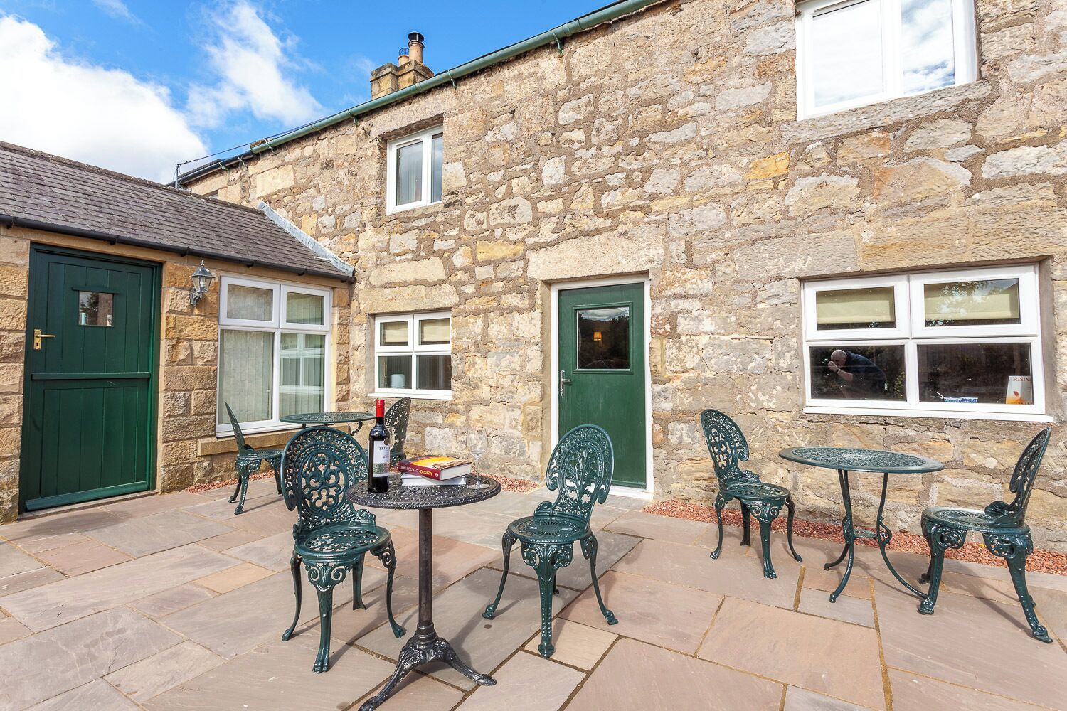 A stone building with a green door, a window, and a table with chairs.