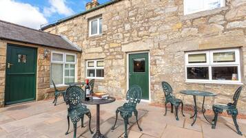 A stone building with a green door, a window, and a table with chairs.