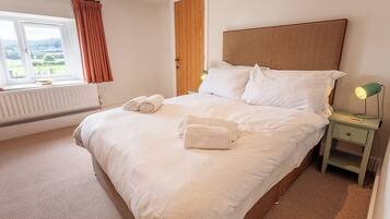A neatly made bed with white linens, a bedside lamp, and a window with curtains.