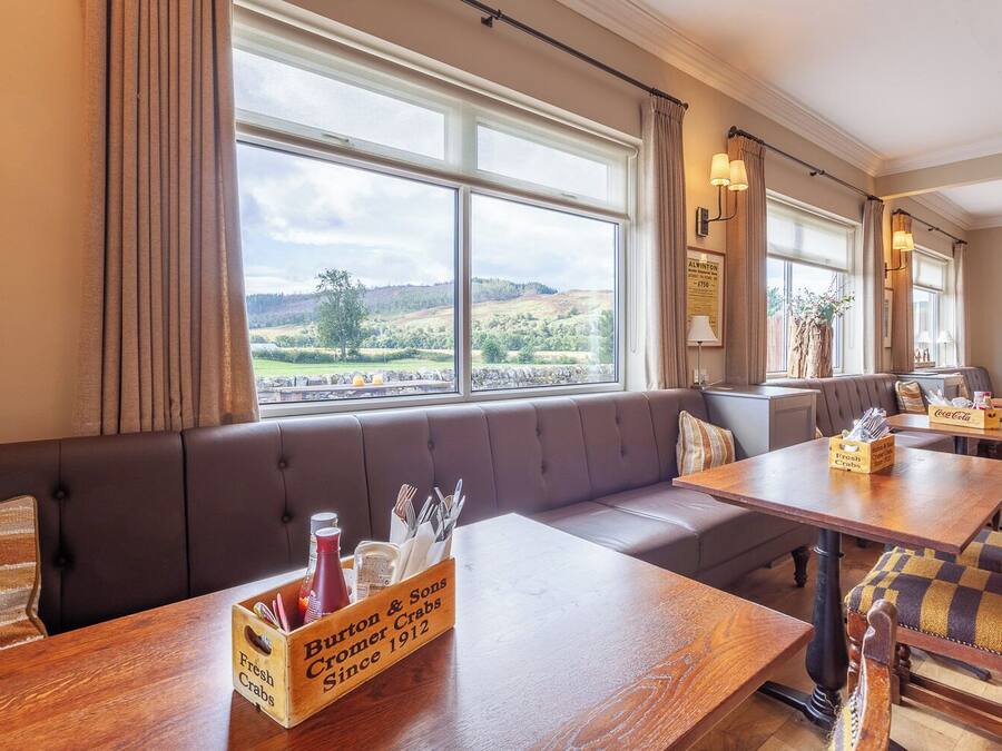 Un restaurante con vistas al campo, que cuenta con un gran ventanal, mesas de madera y un banco acolchado.