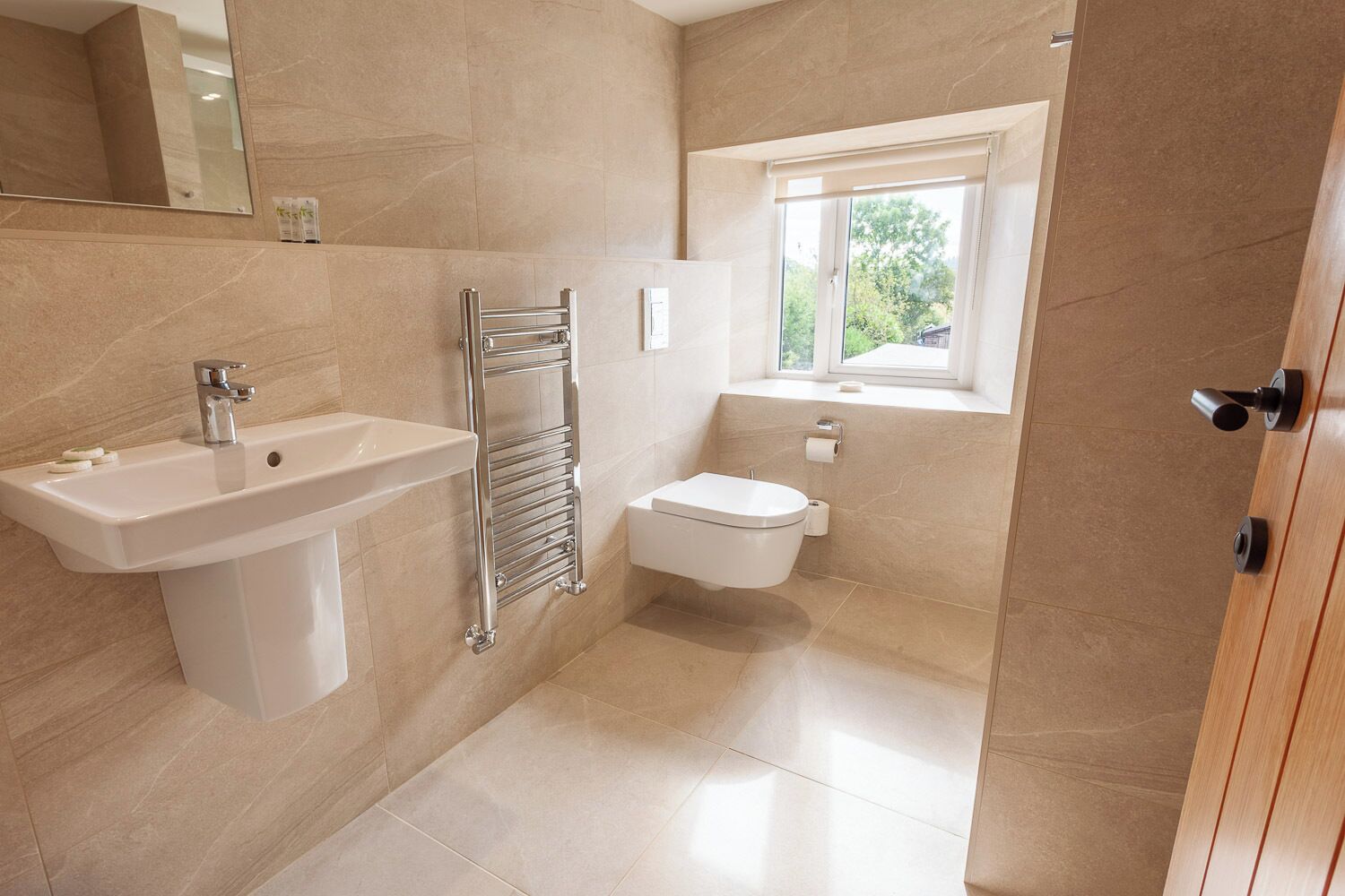 A modern bathroom with a pedestal sink, a towel rack, a toilet, and a window providing natural light.