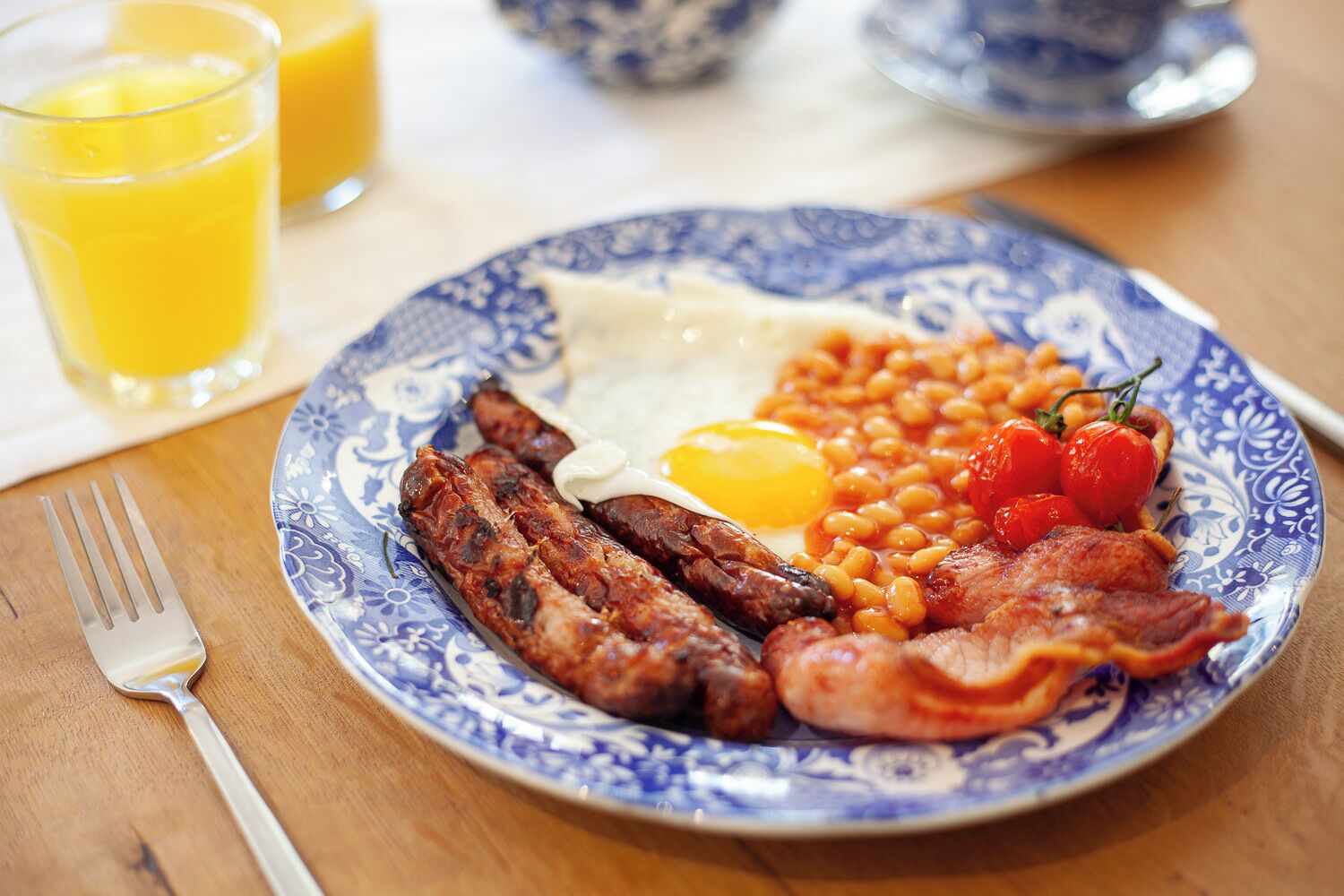 En tallerken med morgenmad, herunder æg, bønner, tomater, bacon og pølser.