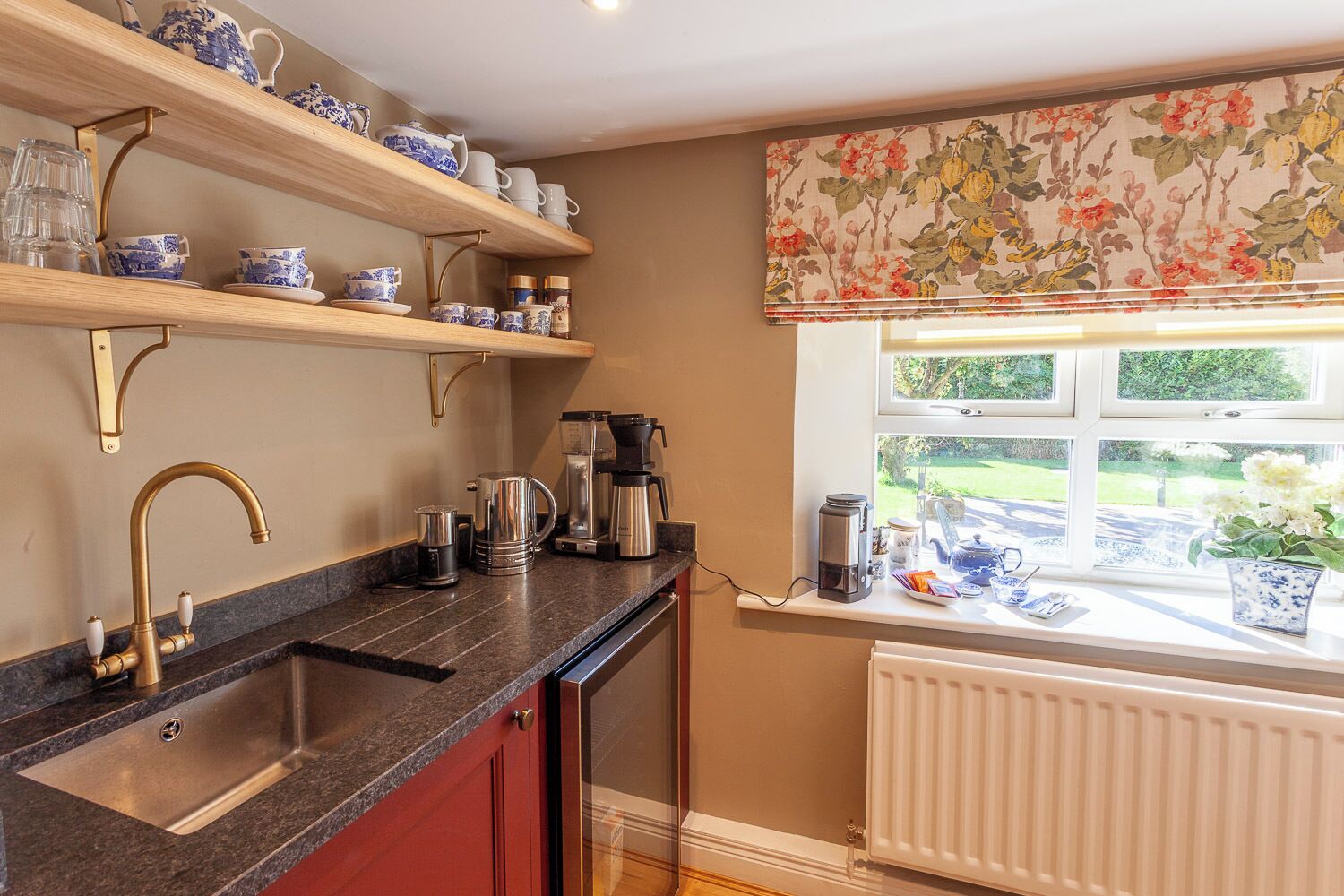 A kitchen with a granite countertop, a stainless steel sink, and a window with a floral valance.