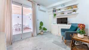 A living room with a TV, a blue sofa, a coffee table, and a dining area with chairs and a table. - MalagaSuite Terrace&Parking Stay Fuengirola (Fuengirola)