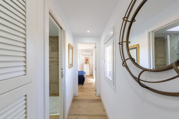 A hallway with a wooden floor, white walls, and a door leading to a bedroom with a blue bedspread.