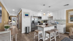 A modern kitchen with white cabinetry, a stainless steel refrigerator, and a central island with stools. - 1st Floor-Pool-Short, Easy Walk to Beach & Restaurants-Seacove 6A🌊 (MIRAMAR BEACH)