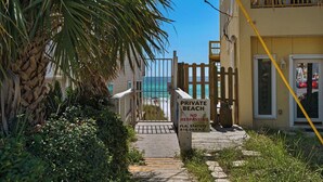 A private beach entrance with a gate, a palm tree, and a building in the background. - 1st Floor-Pool-Short, Easy Walk to Beach & Restaurants-Seacove 6A🌊 (MIRAMAR BEACH)