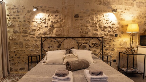 A bed with a stone wall backdrop, two bedside tables with lamps, and towels on the bed. - Charming Provençal studio with peaceful patio. Alpilles (Eyragues)