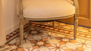 A chair with a cushion in a room with patterned floor tiles and a wooden door. - Charming Provençal studio with peaceful patio. Alpilles (Eyragues)