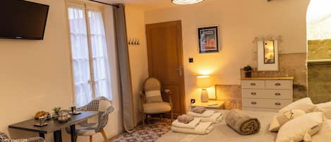 Een hotelkamer met een bed, een bureau met stoelen, een televisie, een lamp en een dressoir.