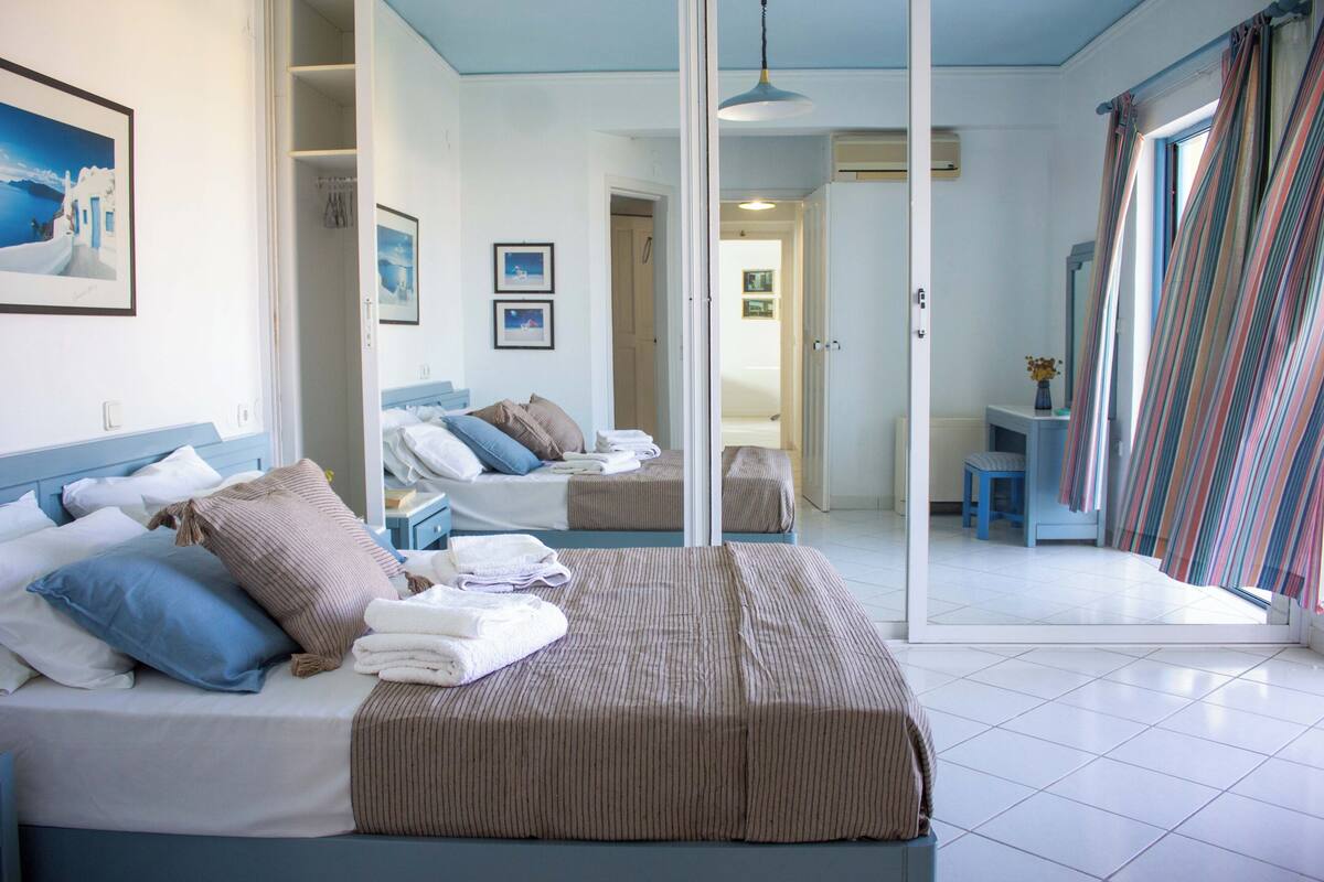 Quarto de hotel com uma cama grande, um espelho e vista para o mar pela janela.