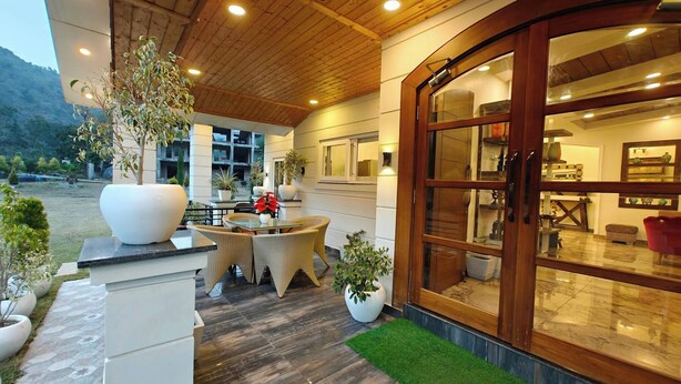 A covered outdoor area with a wooden ceiling, a glass door entrance, and potted plants. - The Paradise - Luxury 3BR Villa Near the Airport in Dehradun (Rishikesh)