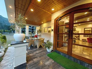 A covered outdoor area with a wooden ceiling, a glass door entrance, and potted plants. - The Paradise - Luxury 3BR Villa Near the Airport in Dehradun (Rishikesh)