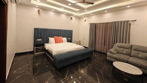 A modern bedroom with a large bed, a sofa, a small round table, and a ceiling fan. - The Paradise - Luxury 3BR Villa Near the Airport in Dehradun (Rishikesh)