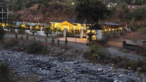 A modern hotel with a well-lit entrance, surrounded by a landscaped garden and a rocky terrain. - The Paradise - Luxury 3BR Villa Near the Airport in Dehradun (Rishikesh)