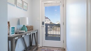 En gang med et træbord, en lampe, et indramet skilt og en dør, der fører til en balkon.