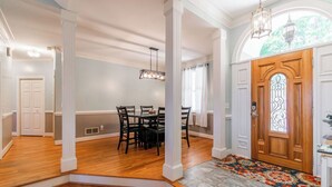A spacious entryway with a wooden door, a dining area with a table and chairs, and a patterned rug.