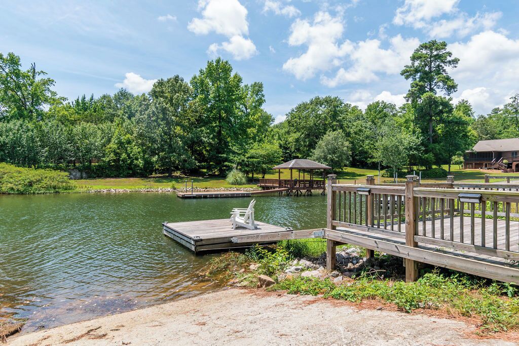 A lakeside dock with a wooden pier, a covered seating area, and a building in the background.