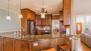 A kitchen with wooden cabinets, granite countertops, a stainless steel refrigerator, and a ceiling fan.