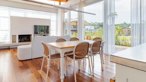 A modern dining area with a wooden table and white chairs, a white sofa, and a fireplace.