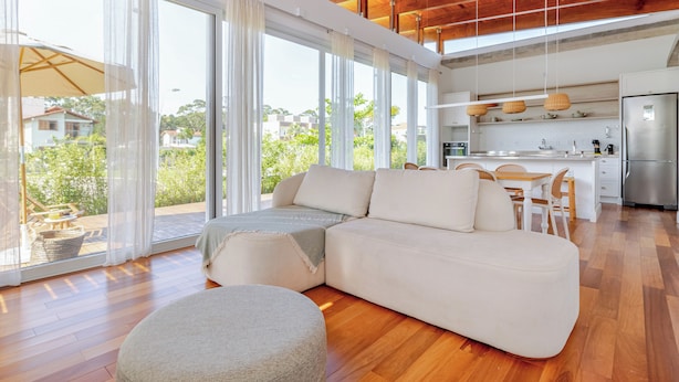 A modern living room with a sectional sofa, a round ottoman, and a dining area with a table and chairs.