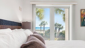 A hotel room with a large bed, a view of the beach, and a window with curtains.