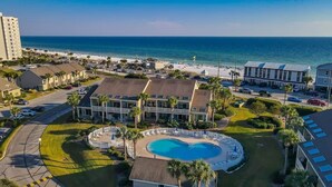 A hotel with a swimming pool, beach view, and parking area.