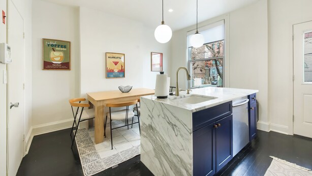 A modern kitchen with a marble island, dark cabinets, pendant lighting, and a cityscape poster on the wall.