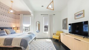 A modern bedroom with a bed, a TV, a mirror, and a view of the city.