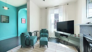 A modern living room with teal walls, a flat-screen TV, a fireplace, and a window with curtains.