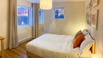 A bedroom with a bed, a nightstand, a hanging light fixture, and two windows.