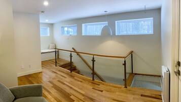 A modern interior with a wooden staircase, a small seating area, and large windows.