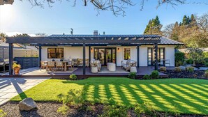 Ein modernes Haus mit Terrasse, Sitzgelegenheiten im Freien und einem gepflegten Rasen.