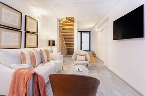 Una sala de estar moderna con un sofá, sillones, una mesa de centro y una escalera con escalones de madera.