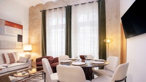 A modern dining area with a round table set for four, surrounded by white chairs. A sofa and a red armchair are positioned against the wall, and a flat-screen TV is mounted on the wall to the right. - Genteel Home Gran Poder II (Seville)