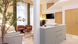 A modern apartment with a living area featuring a sofa, a coffee table, and a potted plant. The kitchen has a countertop, a sink, and a TV mounted above it. - Genteel Home Gran Poder II (Seville)
