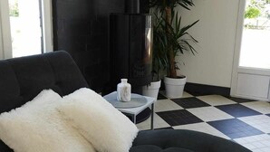 Un saló modern amb un sofà negre, una manta blanca i esponjosa, un vas de ceràmica blanc petit i una planta gran en test.