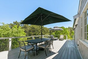 A deck with a table and chairs, an umbrella, and a boat in the background.