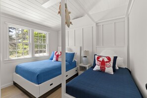 A bedroom with two beds, white walls, a window, and a ceiling fan.