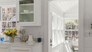Una cocina blanca con armarios de madera, una cafetera y un ventanal con vistas a árboles.