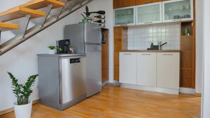 Une cuisine compacte équipée d’un lave-vaisselle encastré, d’un réfrigérateur, de meubles de rangement en bois et d’un escalier.