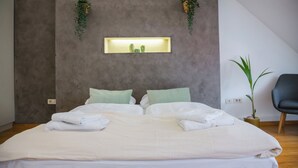 Une chambre moderne avec un grand lit, deux plantes suspendues, une petite collection de cactus et une plante en pot près de la fenêtre.