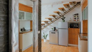 Une cuisine moderne avec des meubles en bois, un réfrigérateur en acier inoxydable, un four à micro-ondes et un four encastré. Un escalier en bois mène à un autre niveau.