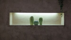 Une étagère rectangulaire sur laquelle sont posés trois cactus verts, le tout adossé à un mur à texture.