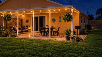 Un área de patio techada con luces colgantes, muebles de exterior y plantas en macetas.