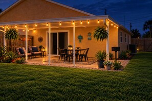 Ein überdachter Patio-Bereich mit Lichterketten, Gartenmöbeln und Kübelpflanzen.